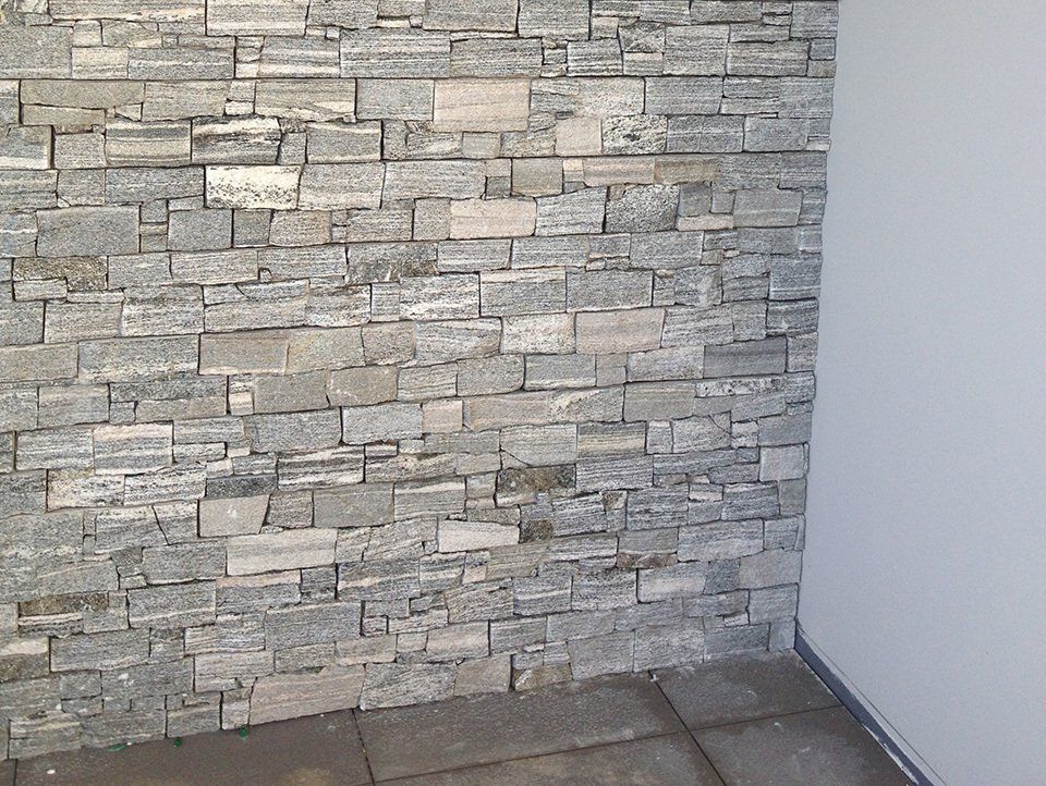 Steinverblendete Wand in Grautönen, neben einer weißen Wand. Dunkler Boden.