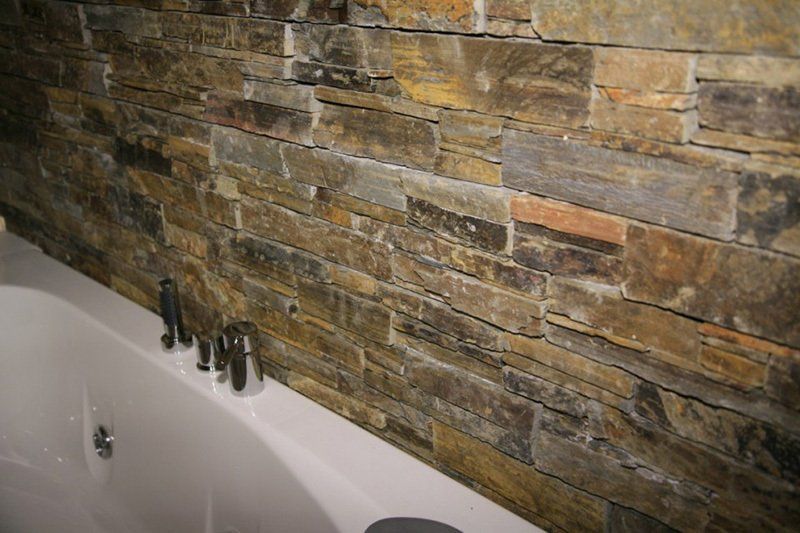 Steinmauer neben einer weißen Badewanne mit silbernen Armaturen.