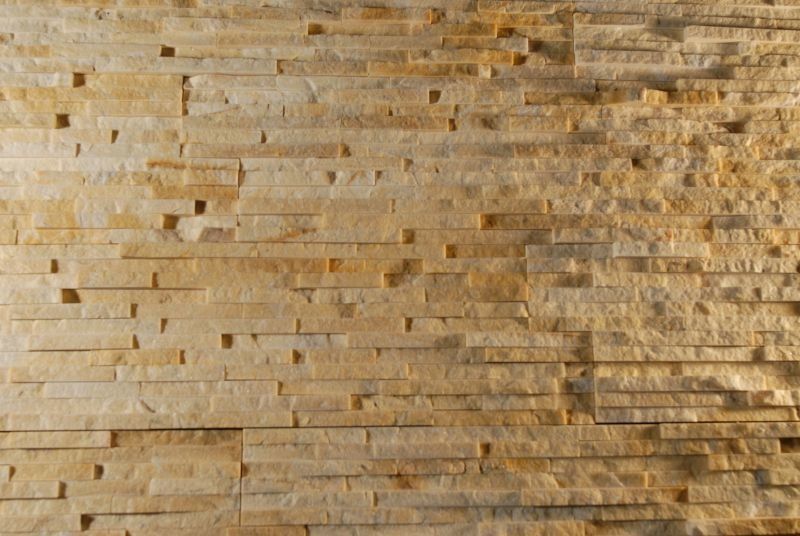 Mauer aus hellbraunem und gelbem Stein mit rechteckigen, strukturierten Blöcken.