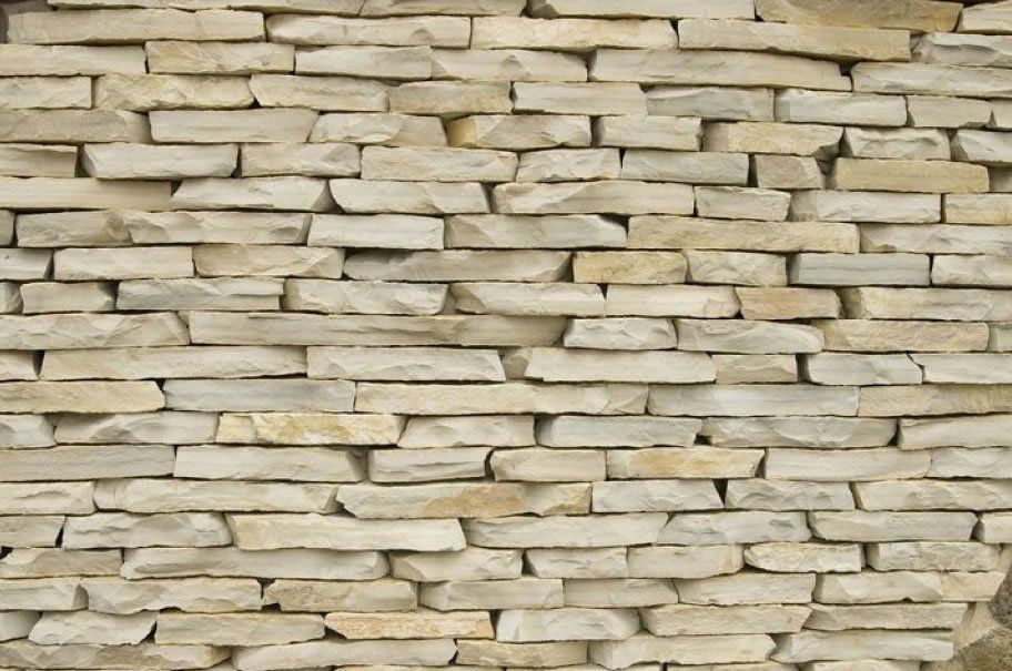 Steinmauer aus hellbeigen und hellbraunen horizontalen Ziegeln.