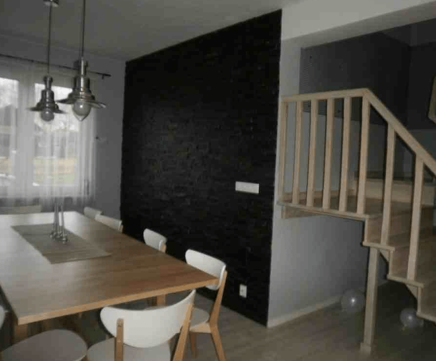 Esszimmer mit Holztisch, weißen Stühlen, schwarzer Wand und Treppe.