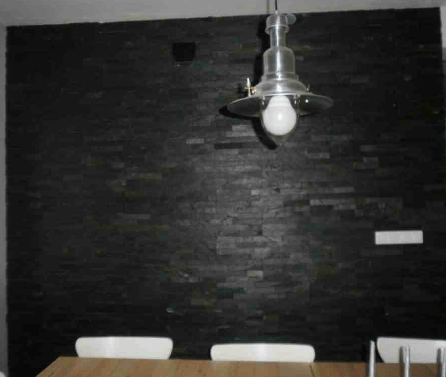Dunkle Steinmauer mit Hängelampe; Tisch und Stühle sind zu sehen.