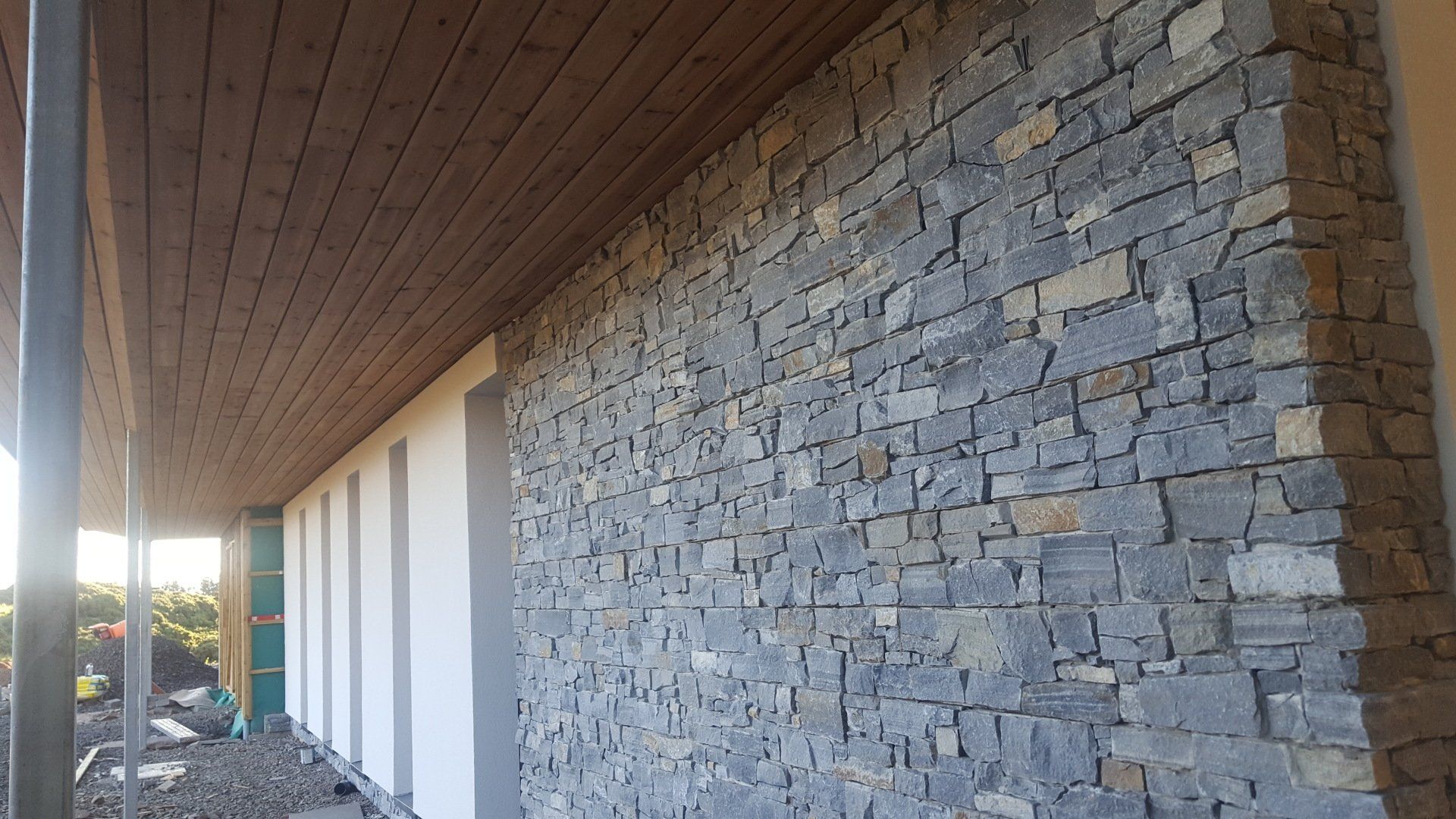 Äußeres Gebäude mit grauer Steinmauer unter einer Holzdecke.