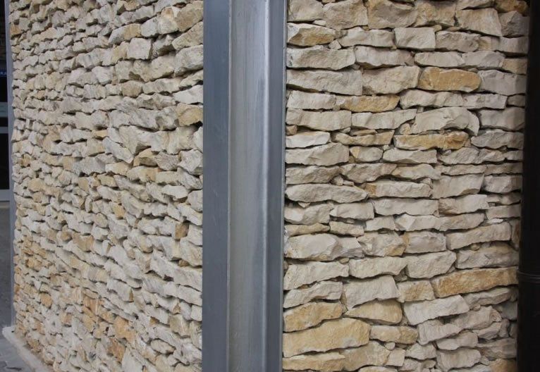 Steinmauern treffen um einen vertikalen Metallträger aufeinander.