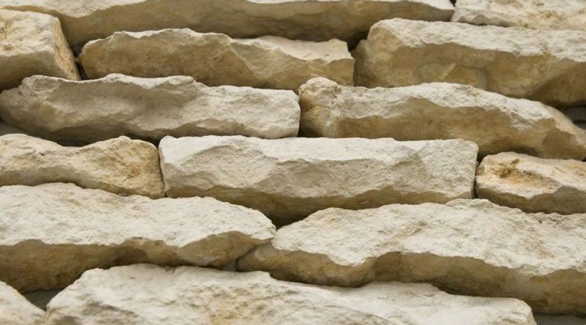 Nahaufnahme von beigefarbenen Steinziegeln, die horizontal gestapelt sind und eine strukturierte Wand bilden.