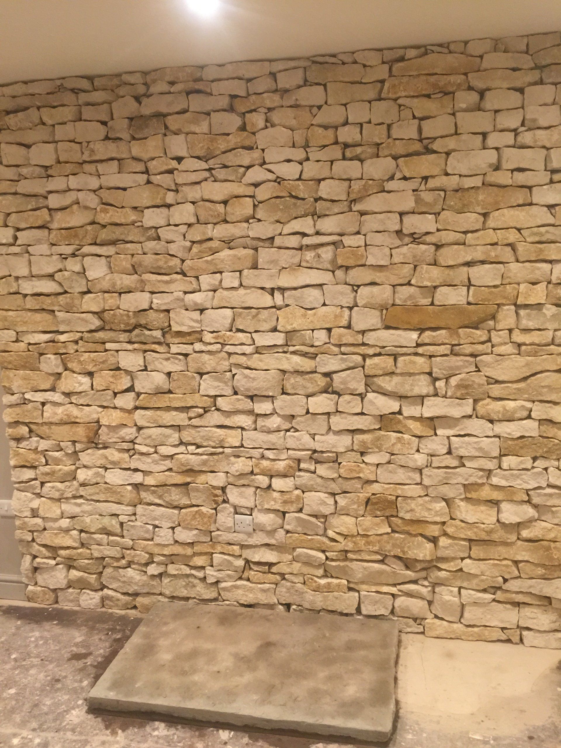 Steinmauer aus hellen, rechteckigen Steinen; am Fuß liegt eine graue Steinplatte.