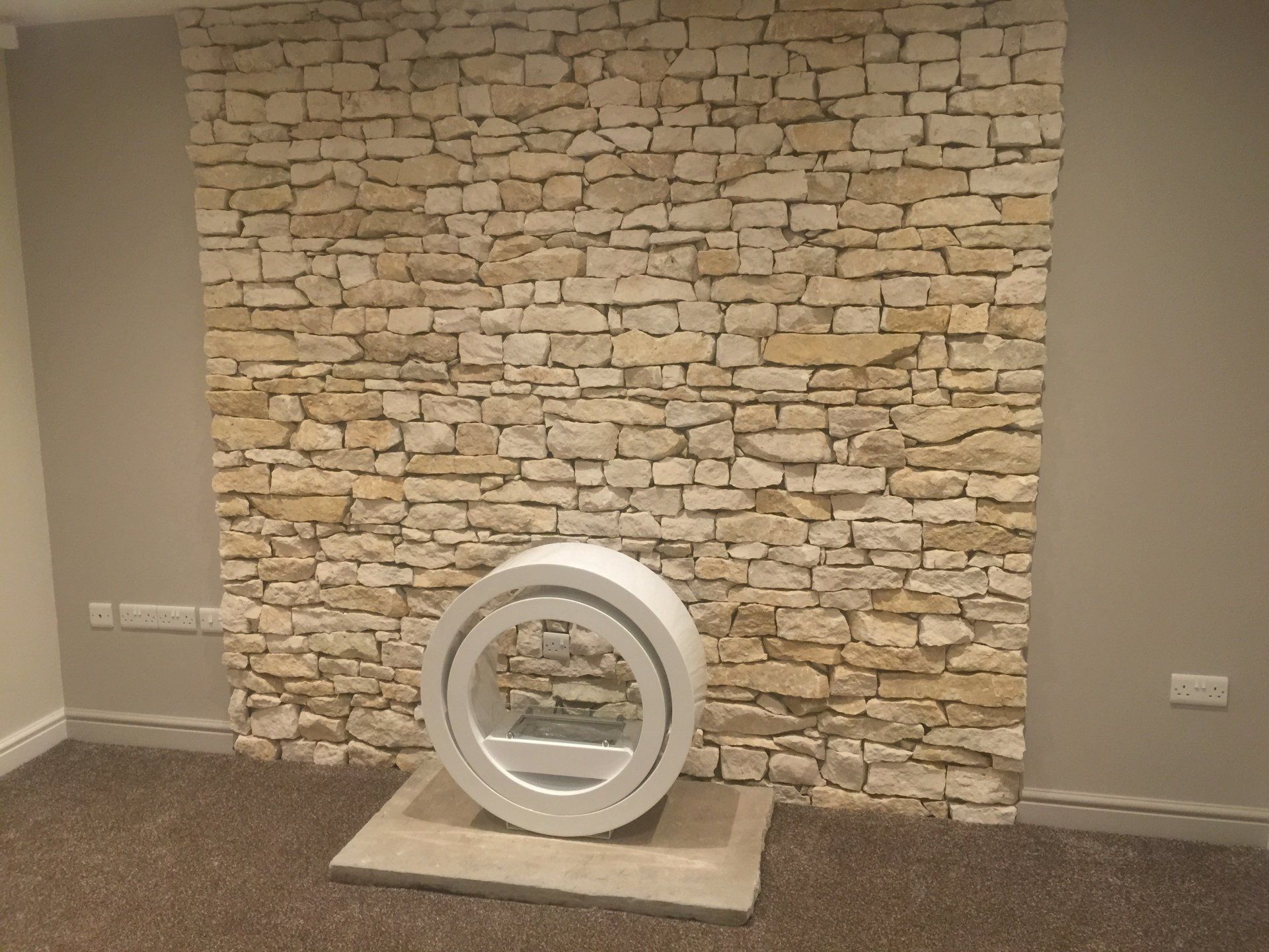 Kamin mit weißer, runder Struktur an einer Steinwand; Teppichboden.