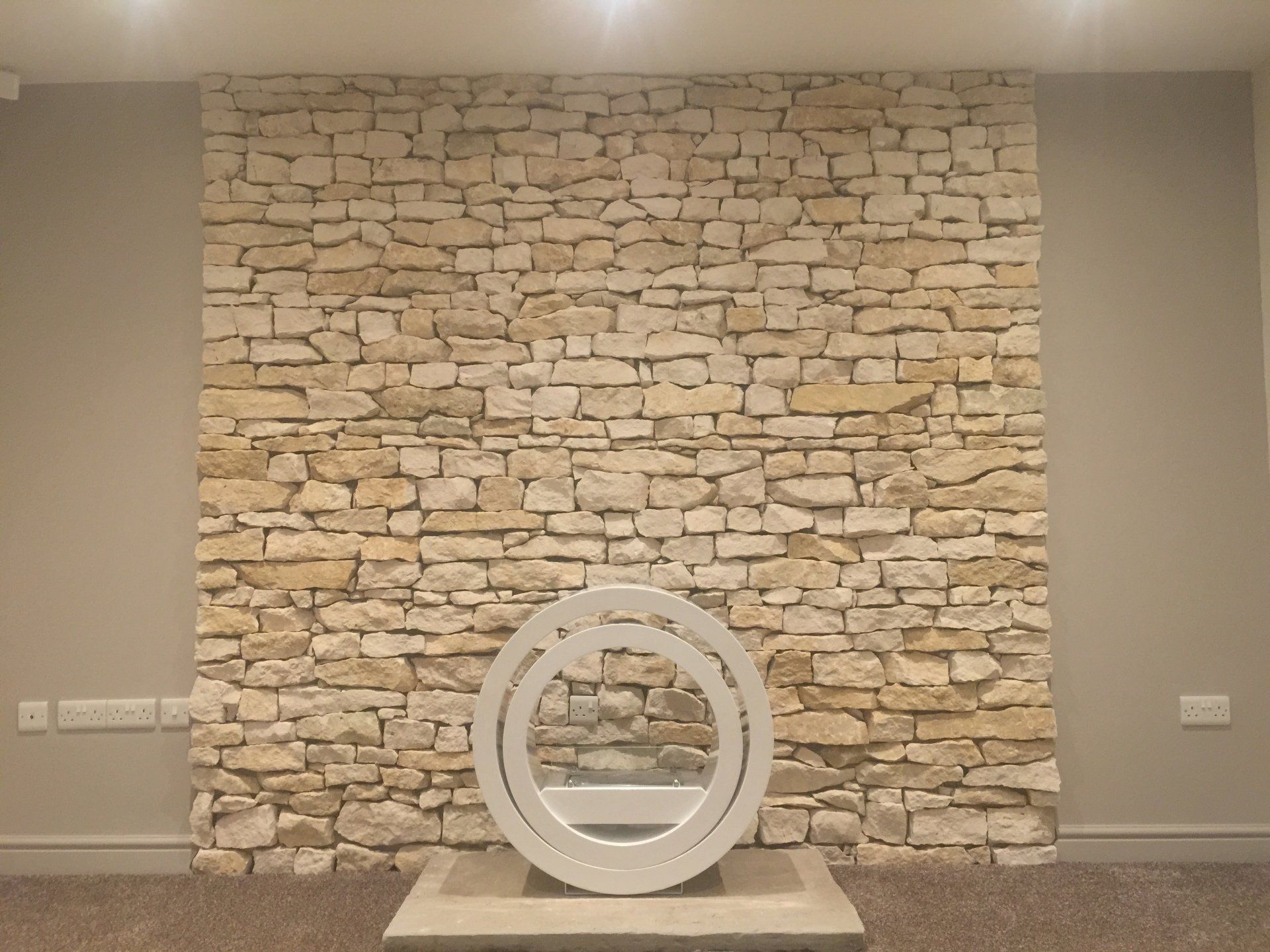 Steinmauer im Hintergrund, davor eine moderne Kunstskulptur.