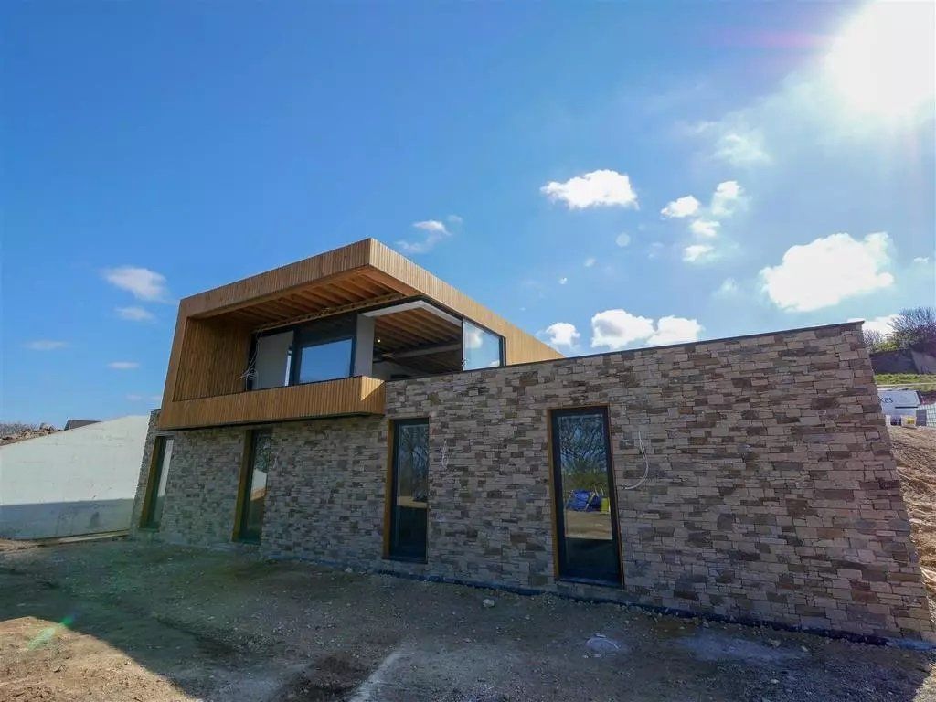 Modernes zweistöckiges Haus mit Steinfassade und Holzelementen vor blauem Himmel.
