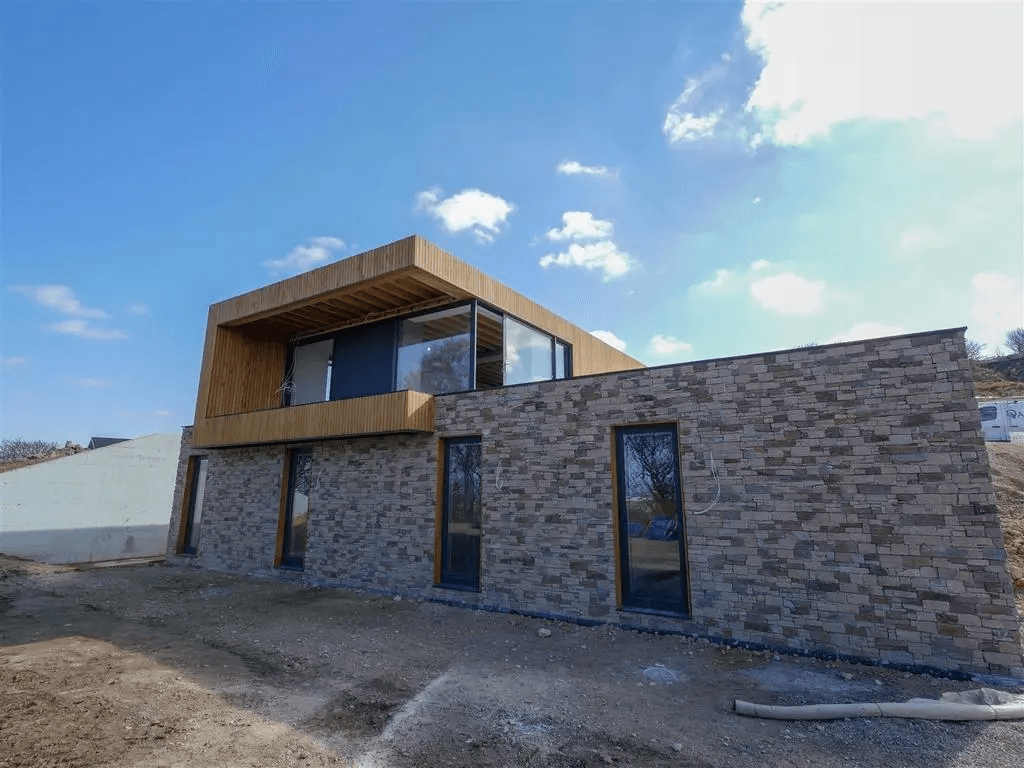 Modernes Haus mit Steinfassade und holzverkleidetem Obergeschoss unter blauem Himmel.