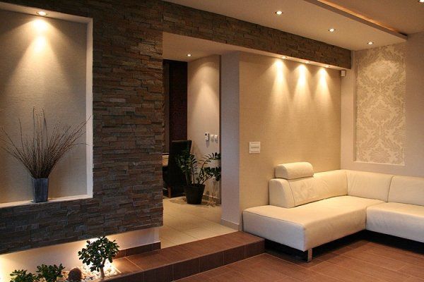 Modernes Wohnzimmer mit neutralen Wänden, Einbauleuchten, einer Akzentwand aus Stein und einem cremefarbenen Ecksofa.