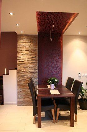 Esszimmer mit dunklem Holztisch und Stühlen, Steinwand als Akzent und gemusterter, bordeauxroter Decke.