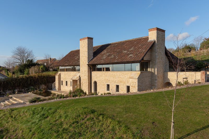 Modernes zweistöckiges Haus mit Backsteinfassade und Ziegeldach, am Hang gelegen, mit Rasenfläche unter blauem Himmel.