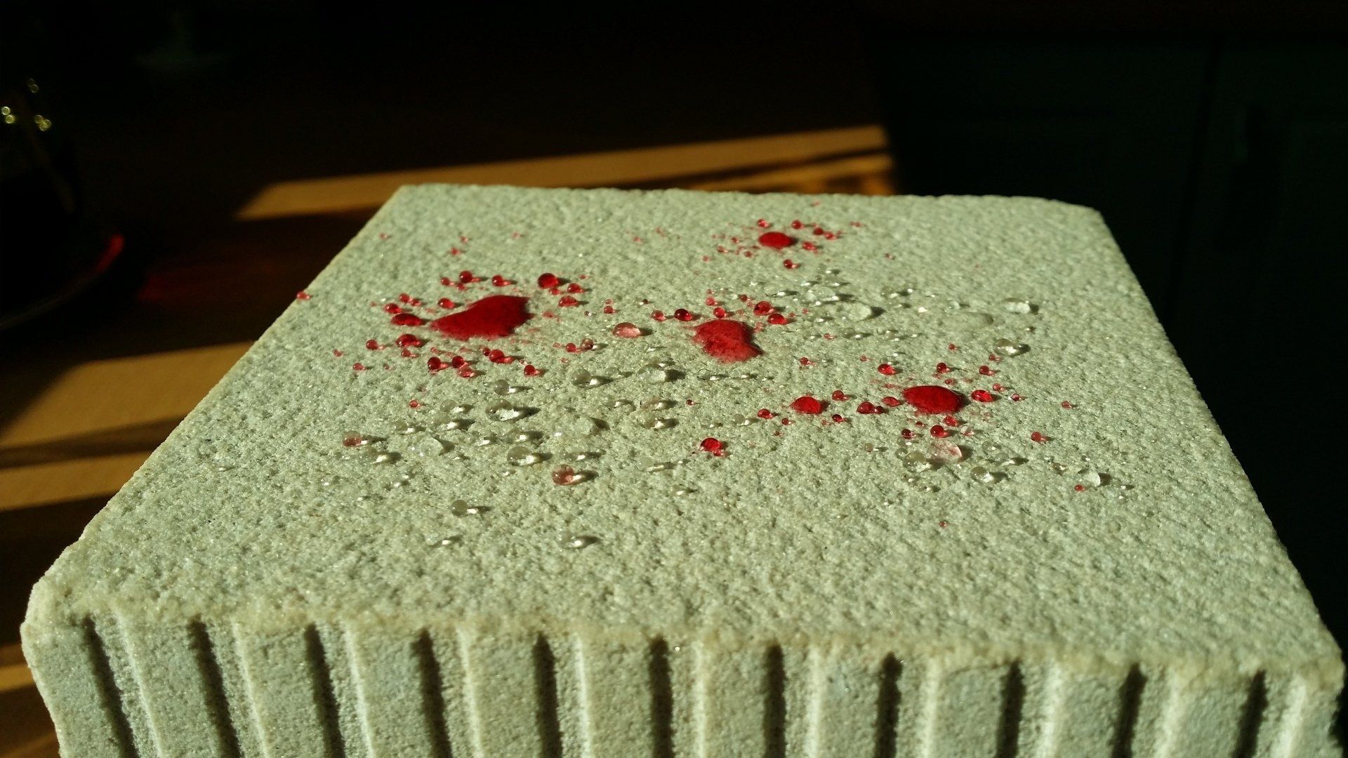 Rote Flüssigkeitstropfen auf einem hellen, porösen Ziegelstein.