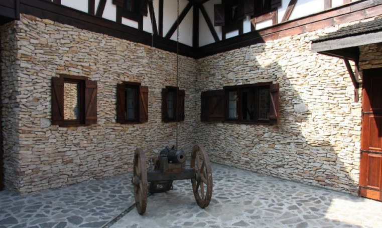 Kanone auf einem gepflasterten Hof mit Mauern aus Stein und Holz sowie hölzernen Fensterläden.