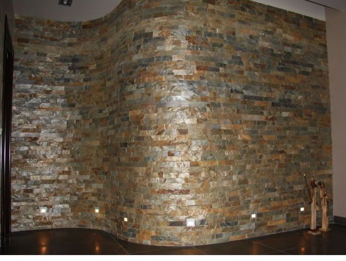 Akzentwand aus Steinziegeln mit geschwungenem Design, beleuchtet durch Bodenleuchten, dunkler Boden.