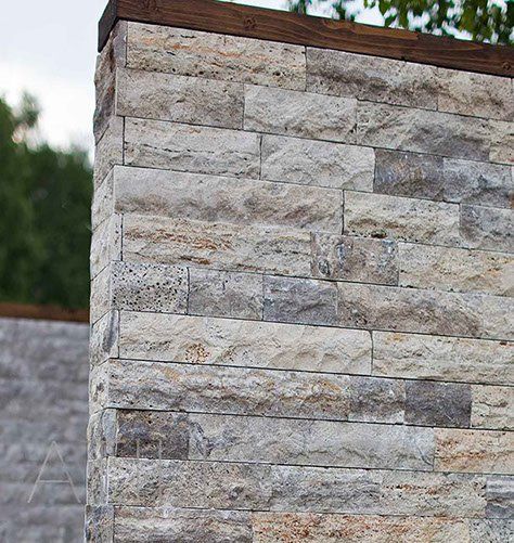 Steinmauer mit Holzabdeckung. Die Ziegel sind grau und beige, im Freien.