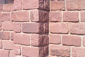 Rote Backsteinmauer mit einer Ecke, Sonnenlicht wirft einen Schatten.