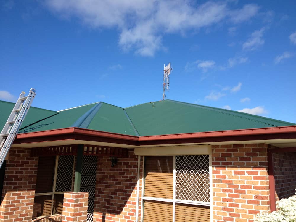 A Brick House With a Green Roof and a Ladder in Front of It — Killiby & Co Roofing Pty Ltd in Tweed, NSW
