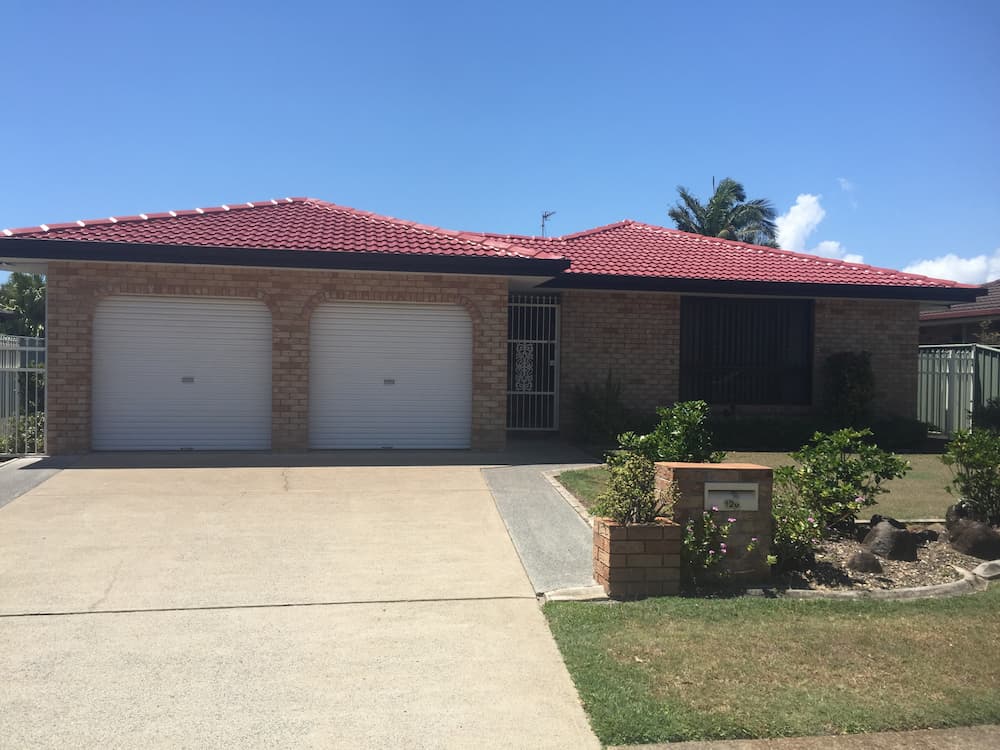 A Brick House With a Red Roof and White Garage Doors — Killiby & Co Roofing Pty Ltd in Tweed, NSW