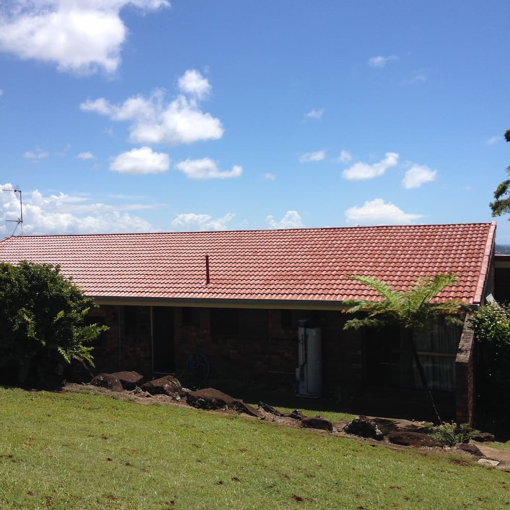 A House With a Red Tiled Roof is Sitting on Top of a Grassy Hill — Killiby & Co Roofing Pty Ltd in Tweed, NSW