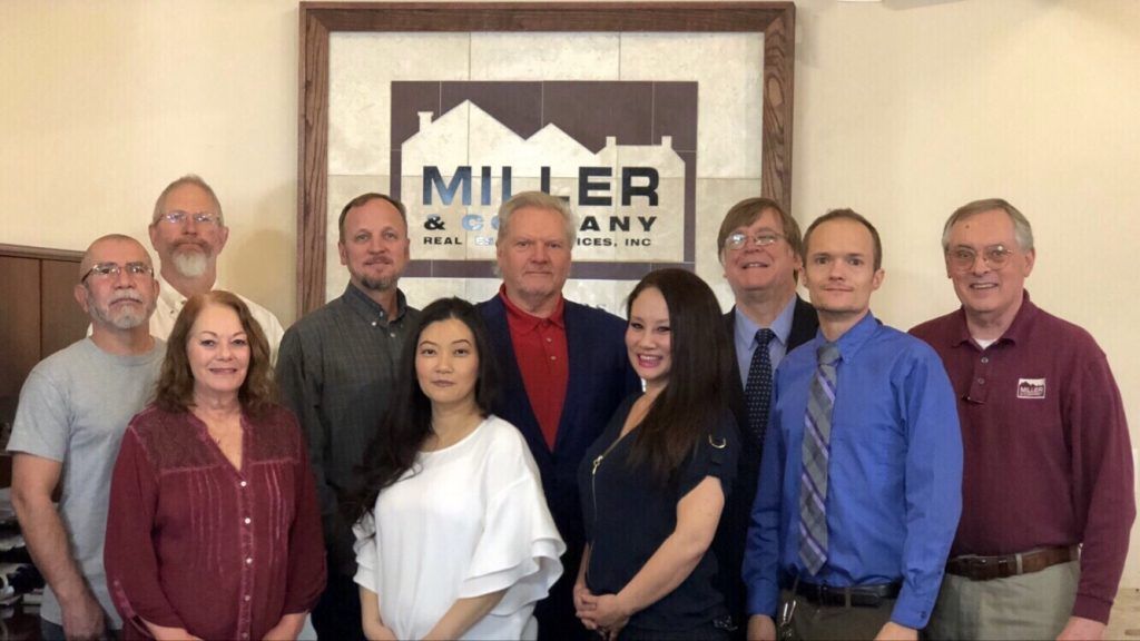 A group of people are posing for a picture in front of a miller company sign.