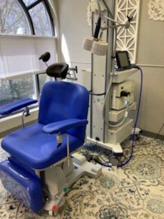 Blue medical chair next to a white machine with screens, in a room with a window.