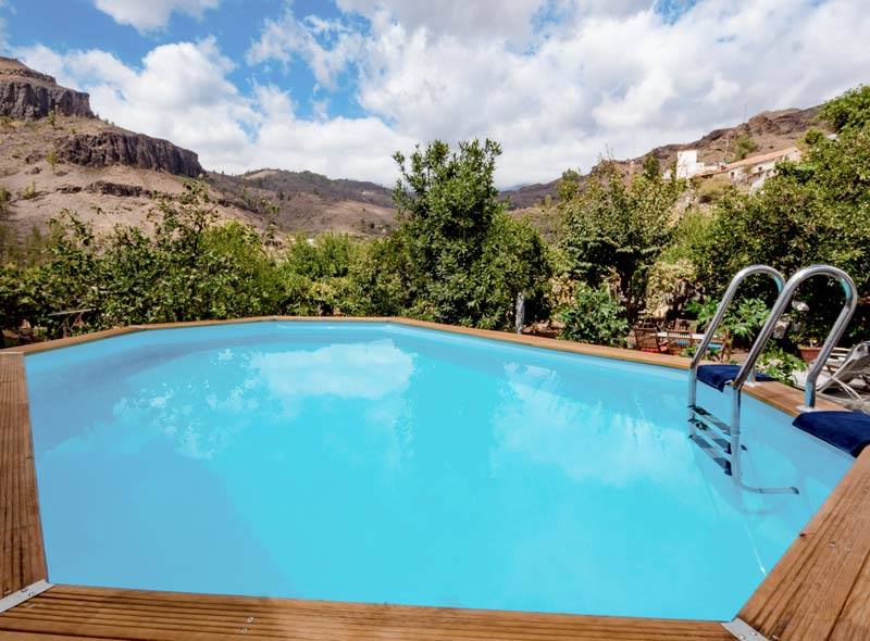 Ein großer Swimmingpool mit Holzdeck und Treppen, umgeben von Bäumen und Bergen.