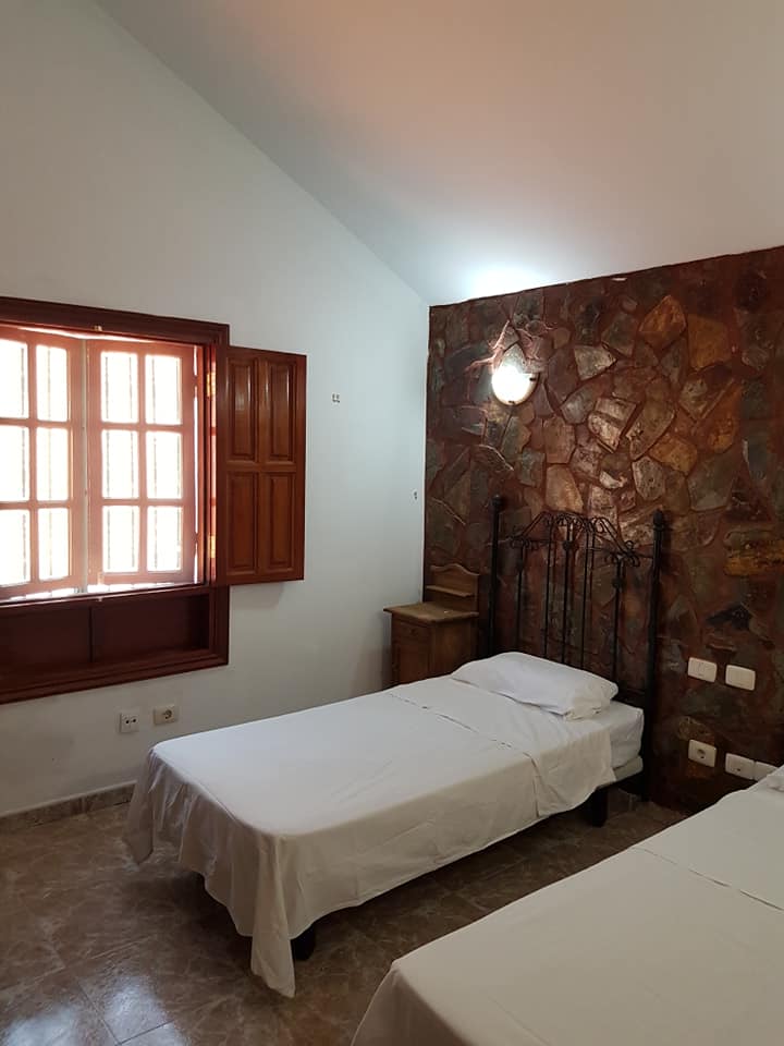 Ein Schlafzimmer mit zwei Betten, einem Fenster und einer Steinwand.