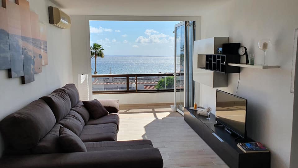 Ein Wohnzimmer mit Couch und Fernseher mit Blick aufs Meer.
