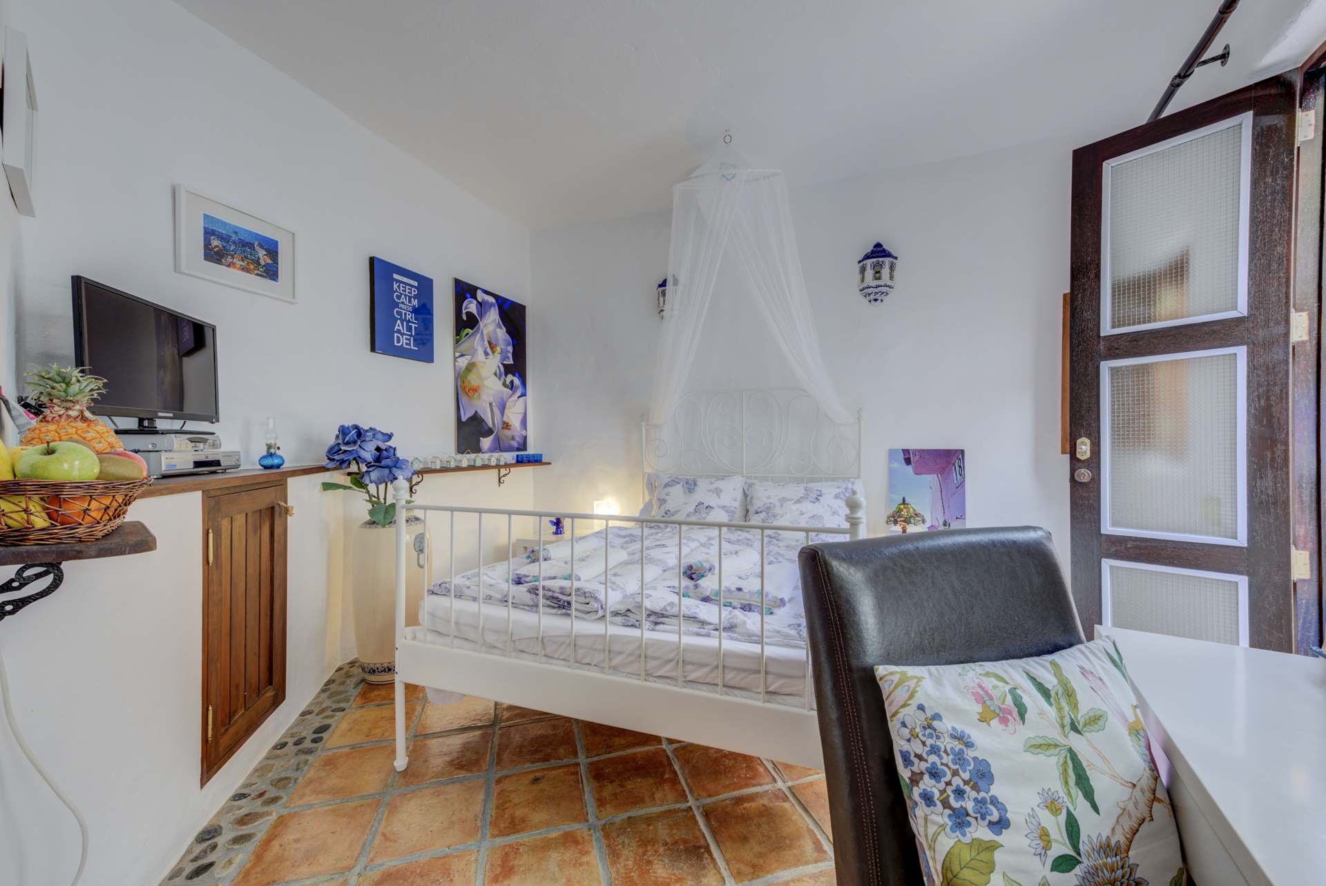 Ein Schlafzimmer mit Bett, Sessel, Fernseher und Himmelbett.
