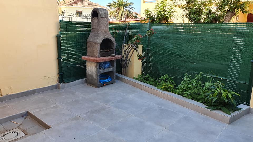 Ein Grill steht auf einer Terrasse neben einem Zaun.