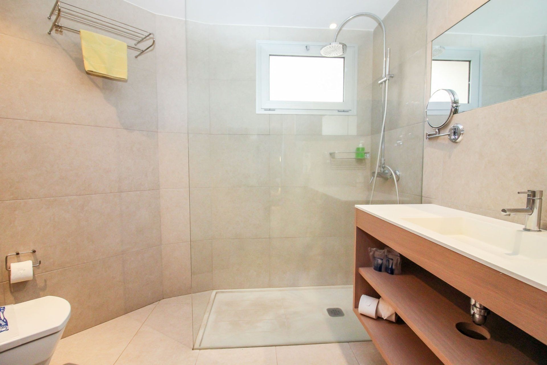 Ein Badezimmer mit ebenerdiger Dusche, Waschbecken, Toilette und Spiegel.