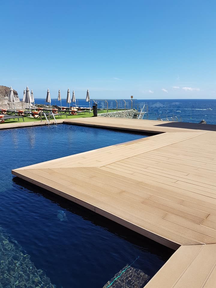 Ein großer Swimmingpool, umgeben von einer Holzterrasse mit Blick auf den Ozean.