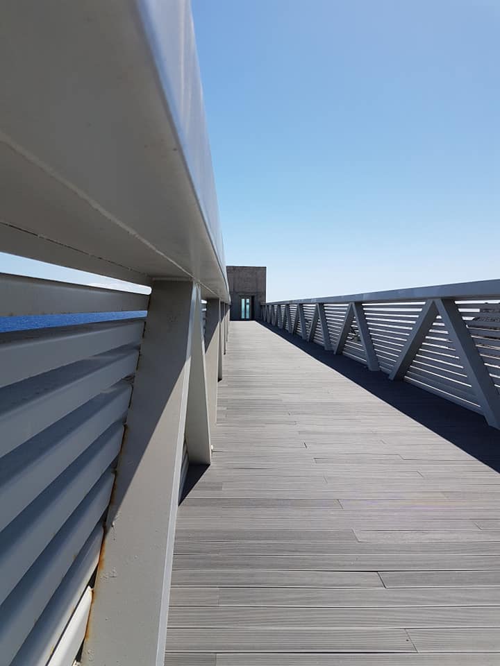 Ein Holzsteg mit einem Metallgeländer und einem blauen Himmel im Hintergrund