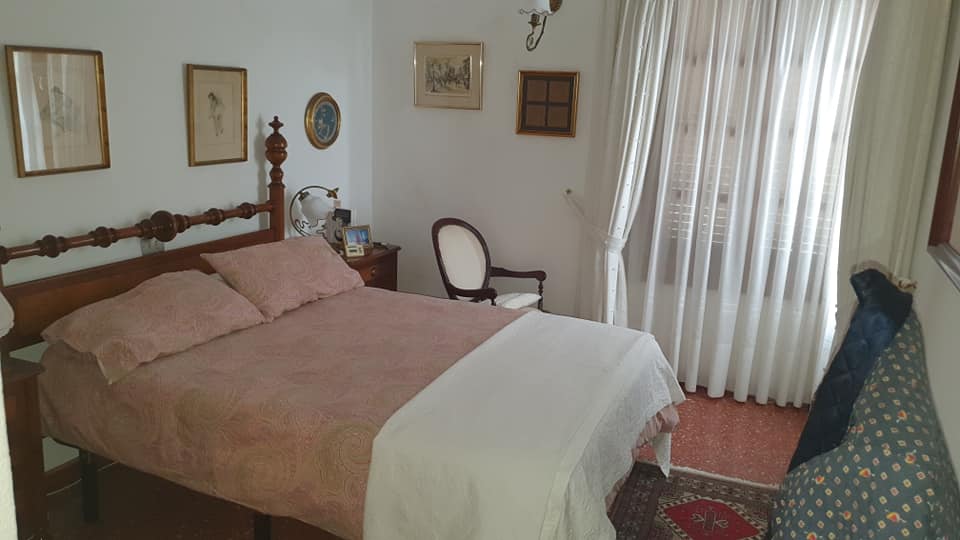 Ein Schlafzimmer mit Bett, Sessel, Nachttisch und Vorhängen.