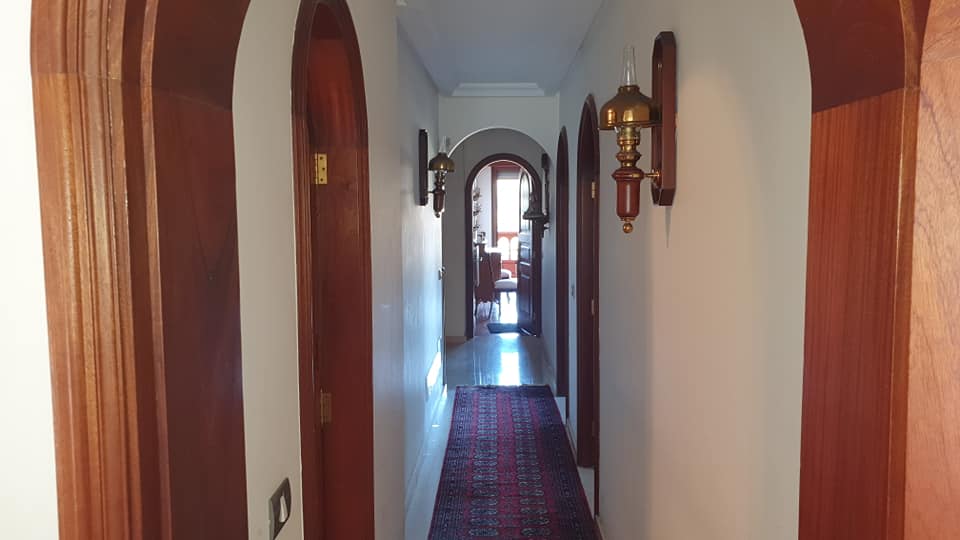 Ein langer Flur mit Bogentüren und einem roten Teppich führt zu einem Wohnzimmer.