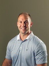 Man with short hair smiling, wearing a blue and white striped polo shirt.