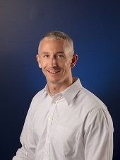 Man in white shirt smiling, blue background.