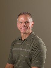 Man with short gray hair and a striped green polo shirt smiling.