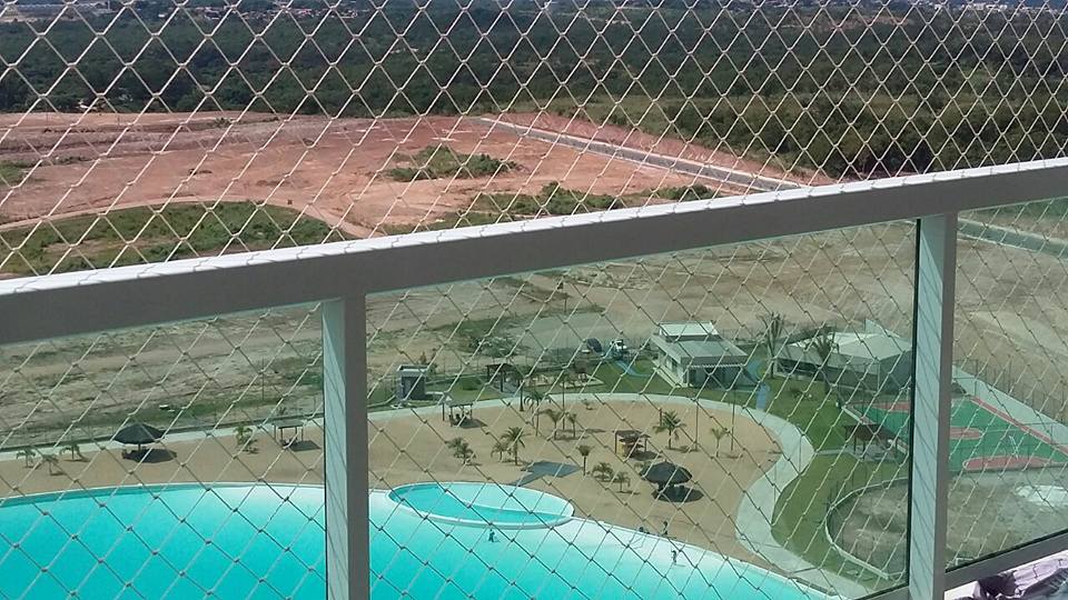 Vista da varanda para uma quadra esportiva cercada, piscina e jardins paisagísticos abaixo.