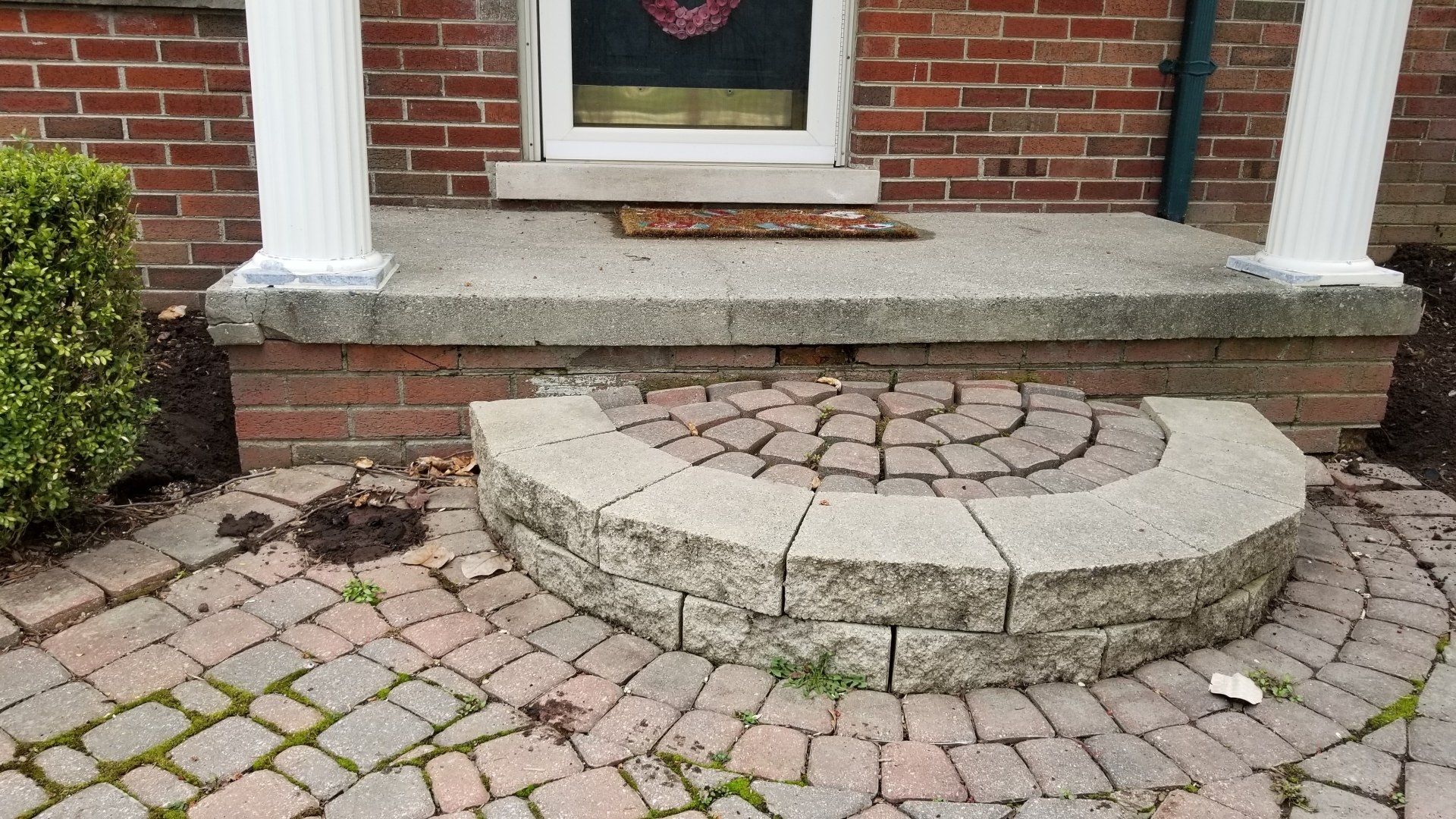A semi-circular stone step leads up to a brick porch with two white columns and a front door.