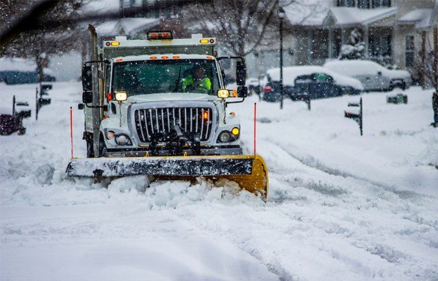 A snowplow clears snow from a residential street during a winter storm.