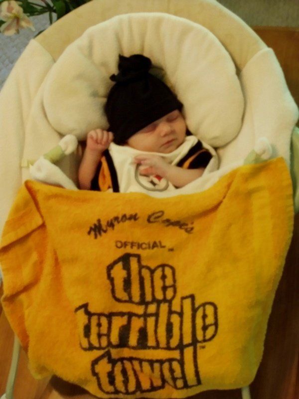 A baby is wrapped in a yellow towel that says the terrible towel