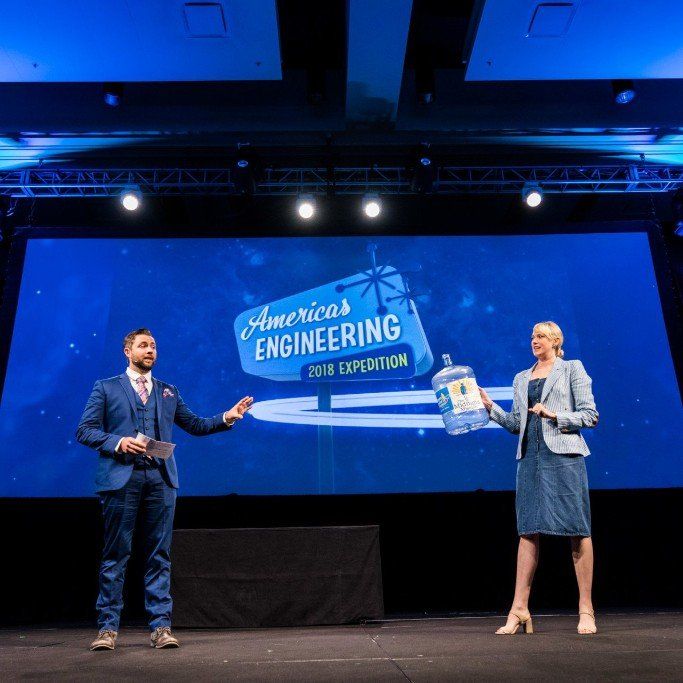 Two presenters onstage beside a large blue screen reading “America’s Engineering 2018 Celebration.”