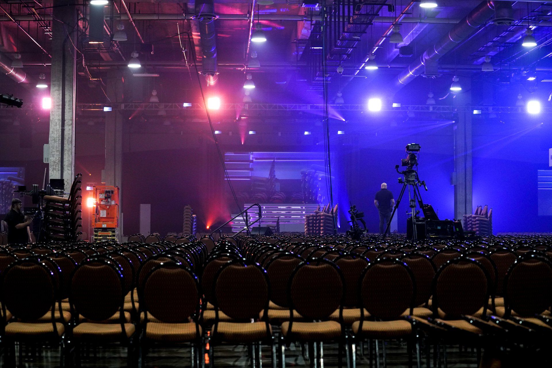 Venue transformation in progress with staging, lighting, and camera systems being installed for a corporate event.