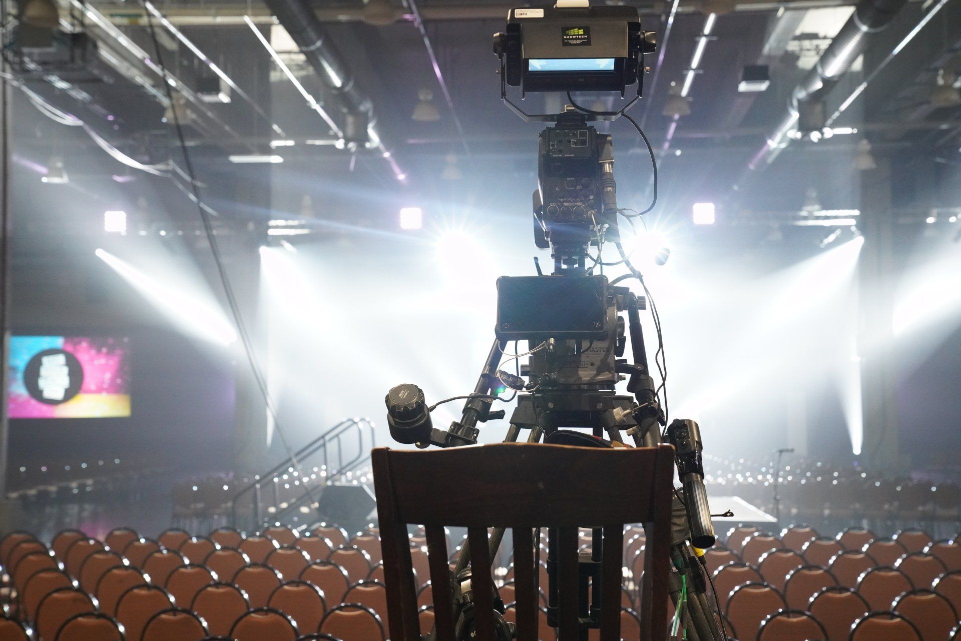 Broadcast camera positioned to capture a live corporate event from the center of the general session.