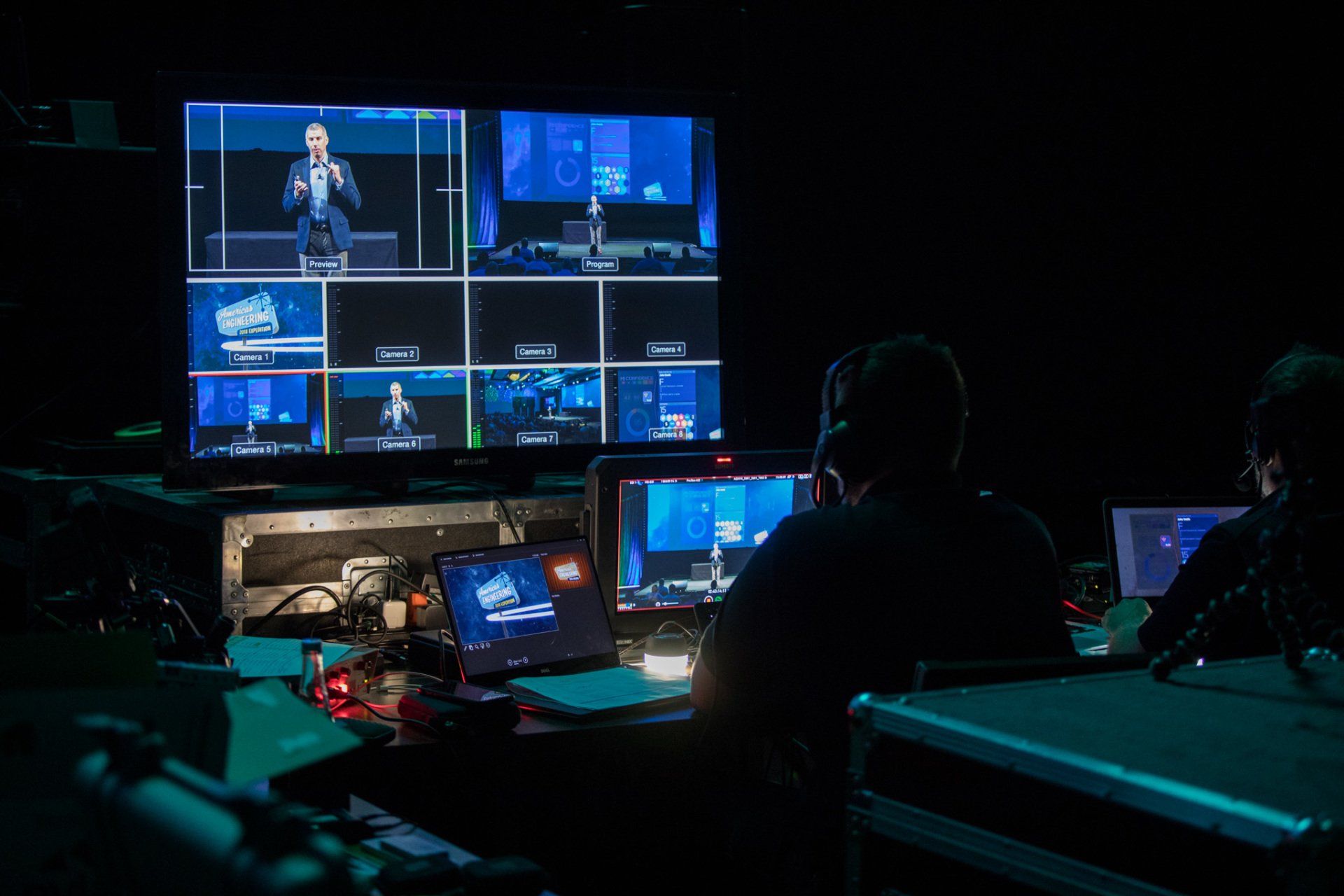 Production team directing a multi-camera live stream from the video control room during a corporate conference.