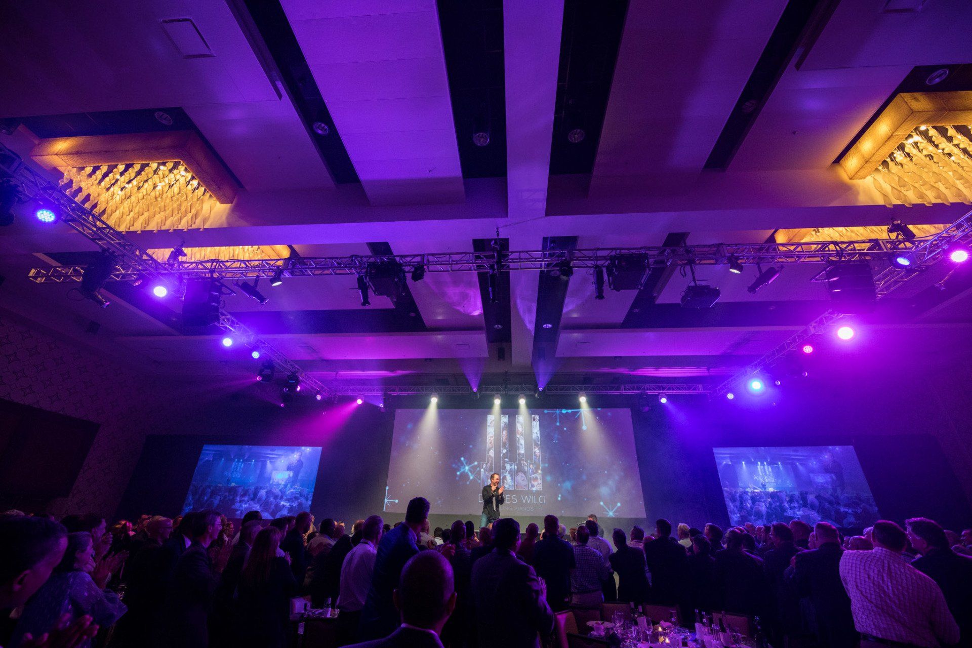 Audience gathered for a high-energy corporate event featuring dynamic stage lighting and large-format presentation screens.
