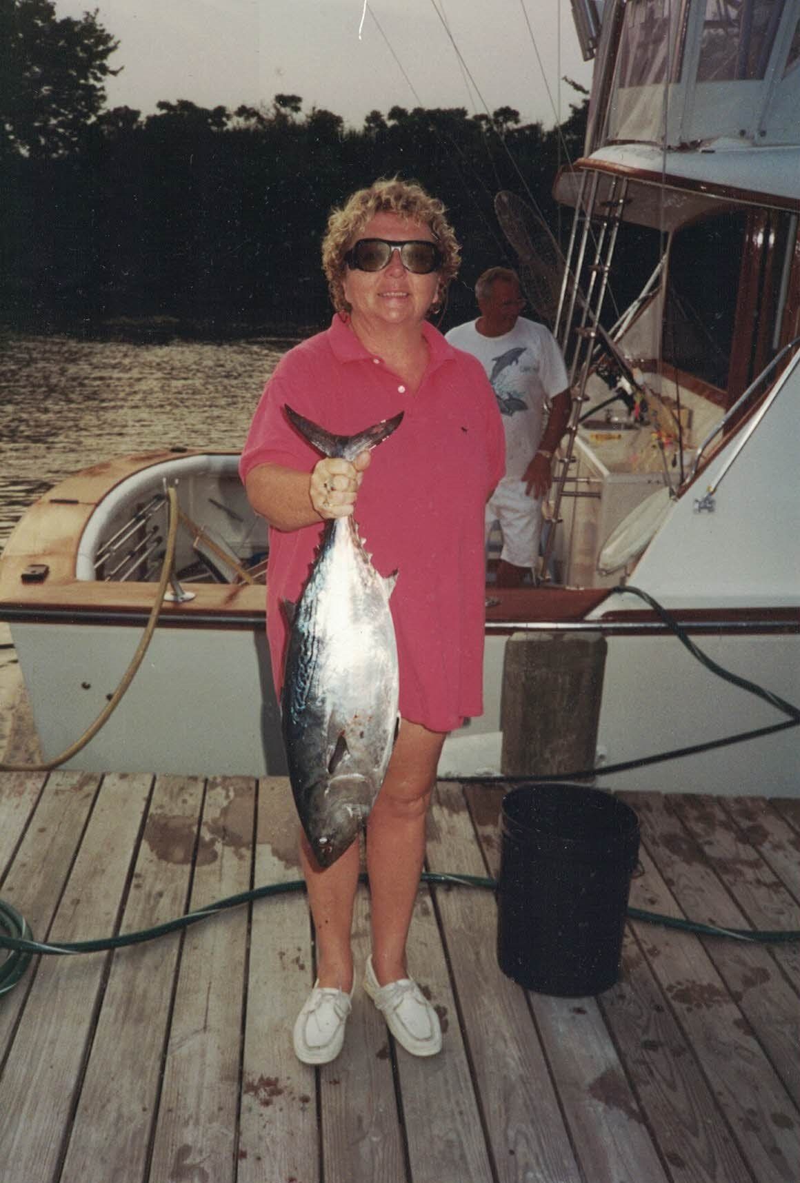A woman in a pink shirt is holding a large fish